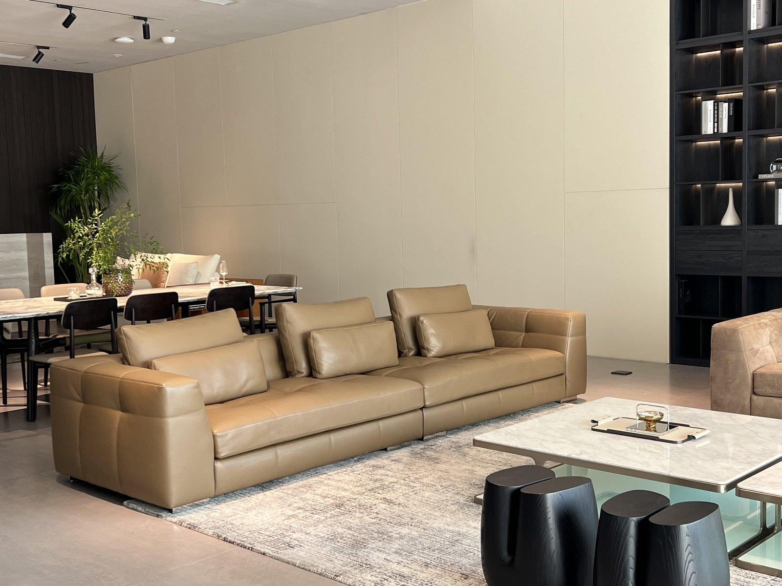 Salón-comedor de villa con sofá modular de cuero color camel, mesa de comedor y estantería de madera a medida.