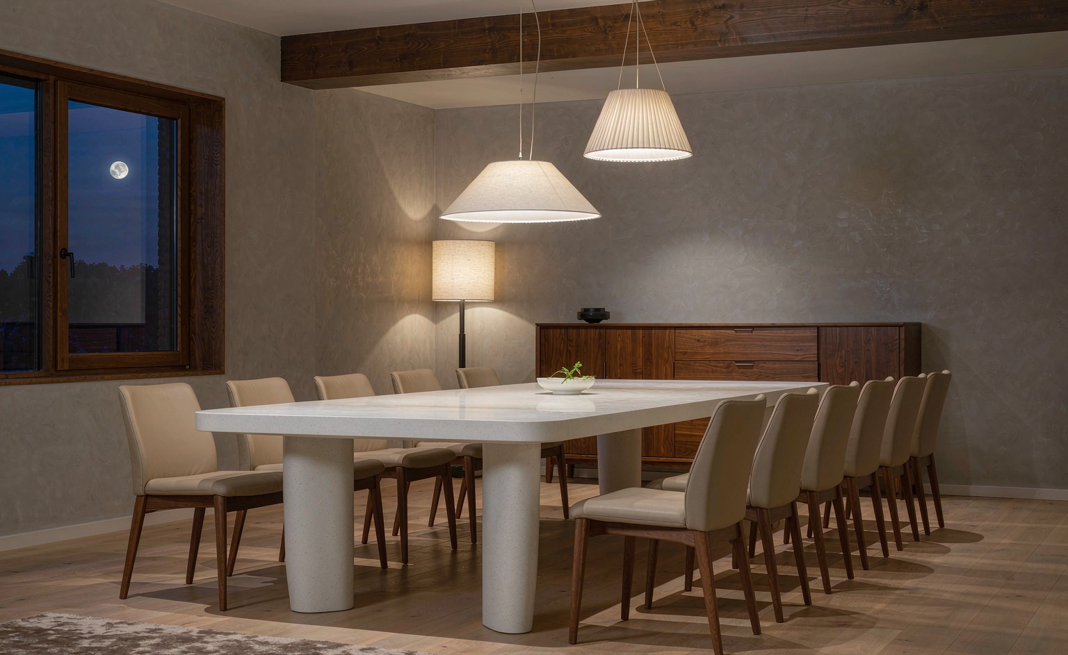 Comedor de una villa con mesa larga de piedra sinterizada, aparador de nogal y lámparas colgantes de luz cálida