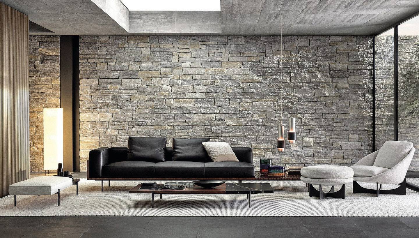 Salón en expositor con sofá de cuero negro, pared de piedra apilada y lámparas colgantes.