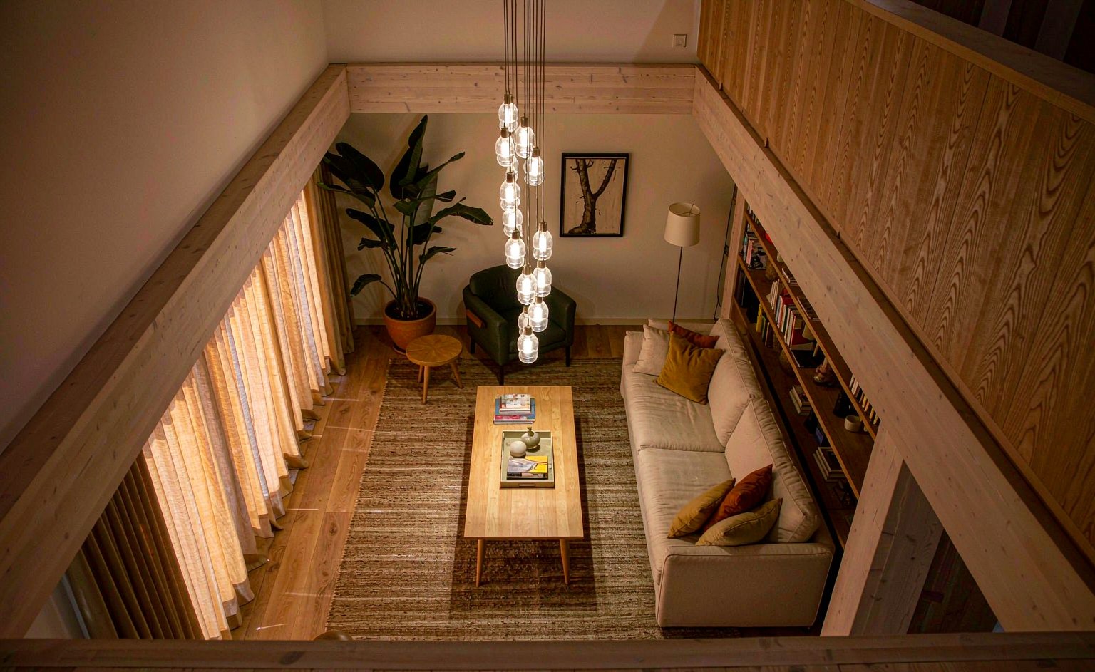 Salón de doble altura visto desde el pasillo superior, con colgante bajo y el remate de la biblioteca de madera