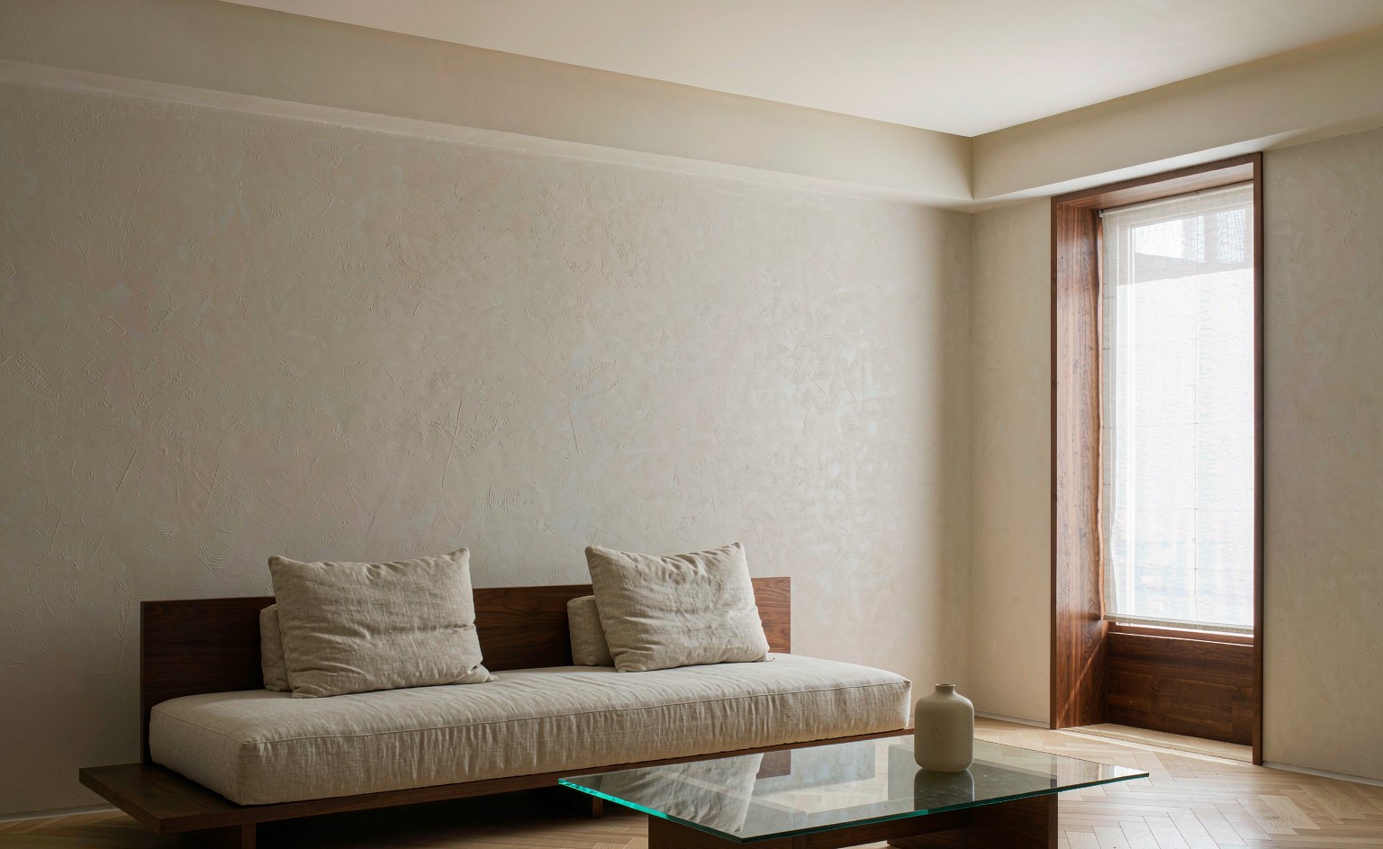 Salón de villa con sofá bajo de gran formato junto a una pared despejada y una ventana lateral