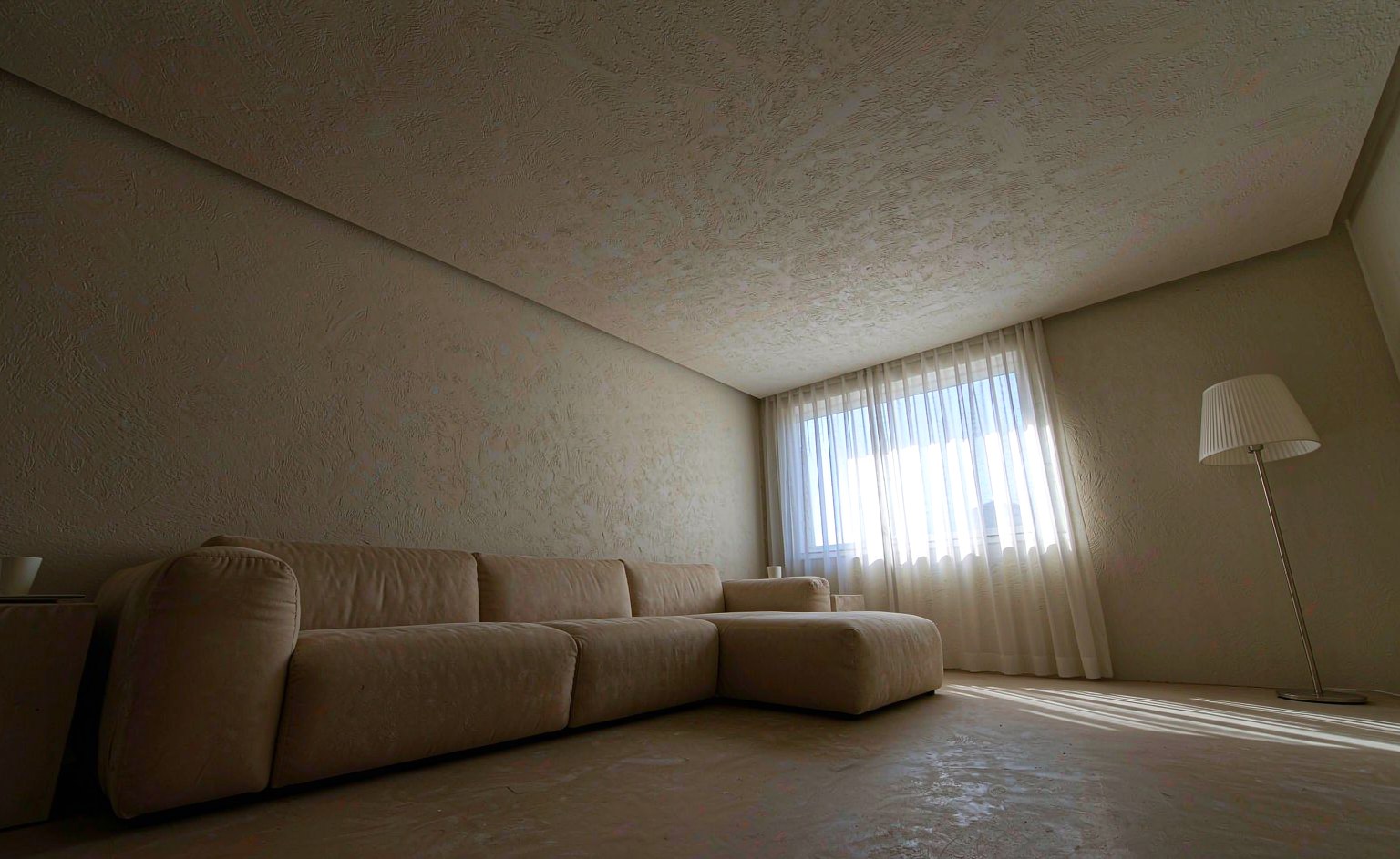 Sofá bajo de gran formato en una sala de techo bajo, con luz lateral y una pared despejada detrás