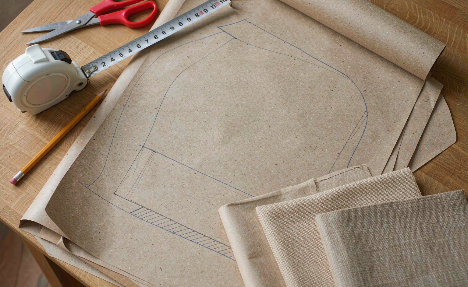 Mesa de taller con el patrón de corte de un asiento, muestras de tapizado, una cinta métrica y un lápiz