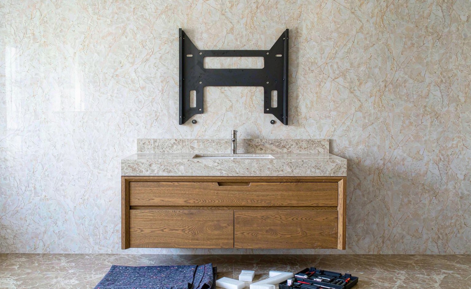Mueble de baño suspendido de roble con encimera de piedra junto a la pared, con soporte de acero, caja de herramientas y manta protectora en el suelo