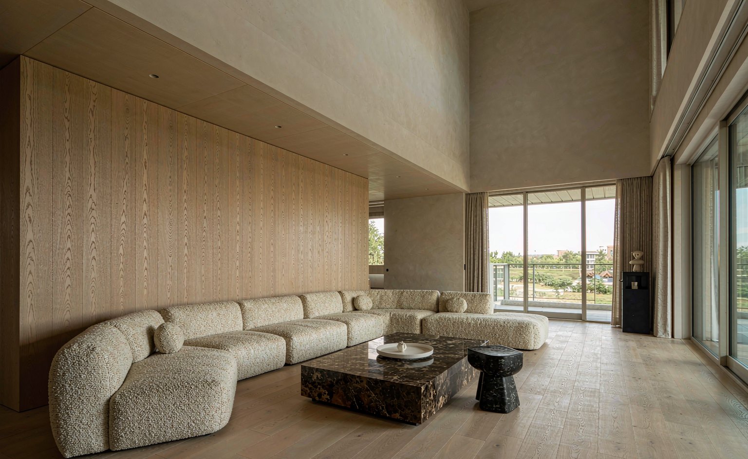 Salón de villa de doble altura con sofá modular de boucle crema y panelado de roble