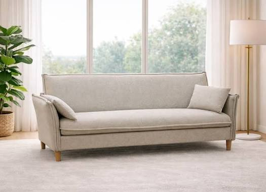 Sofá cama beige claro con cojin junto a ventanal panoramico con plantas verdes y lampara de pie - sala pequena y luminosa