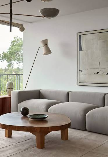 Sofá chaise longue modular gris claro con mesa de centro de madera en sala con lampara de pie y arte abstracto