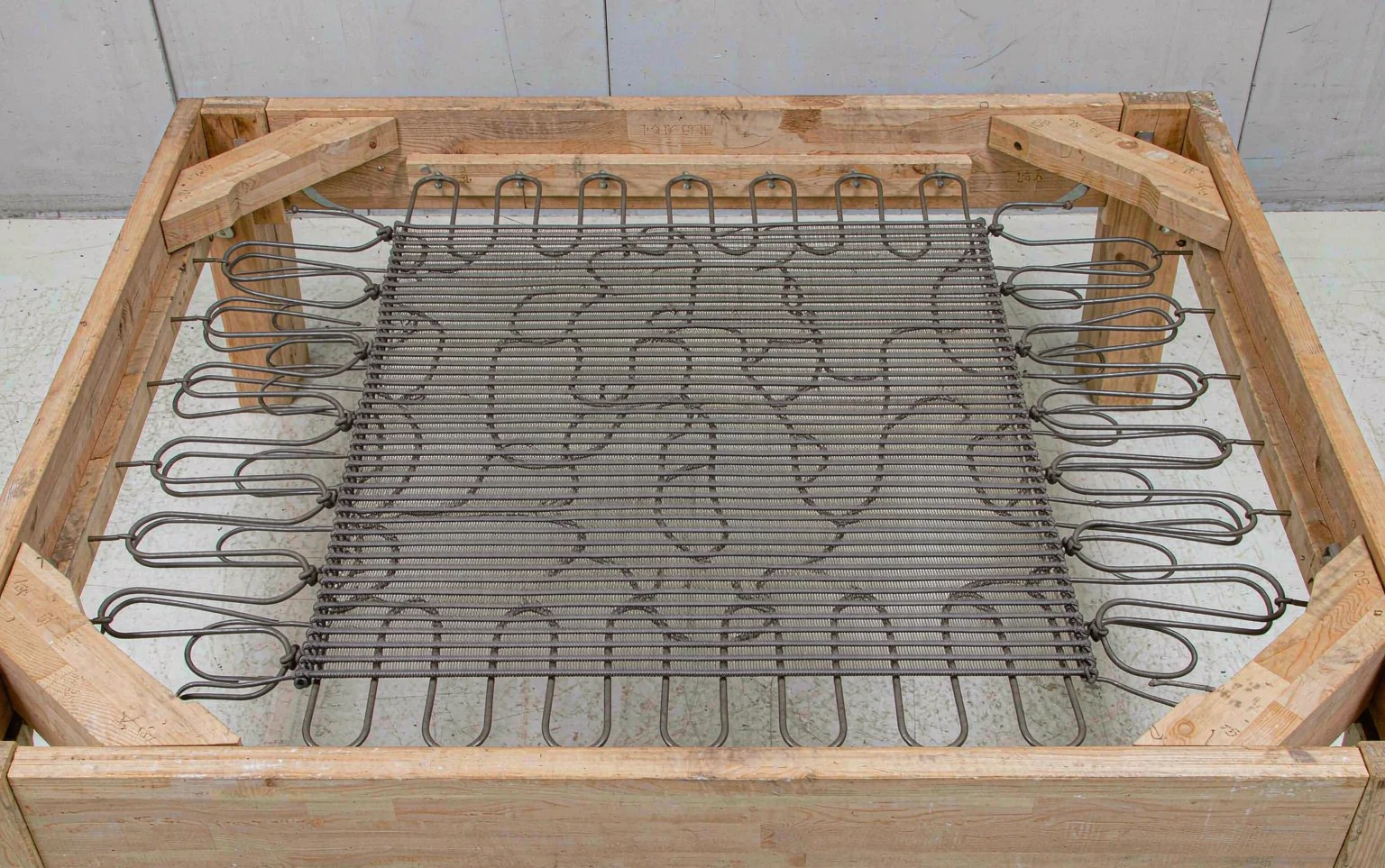 Primer plano del bastidor de un banco tapizado mostrando correas elásticas de webbing y resortes sine en zigzag montados sobre madera seca