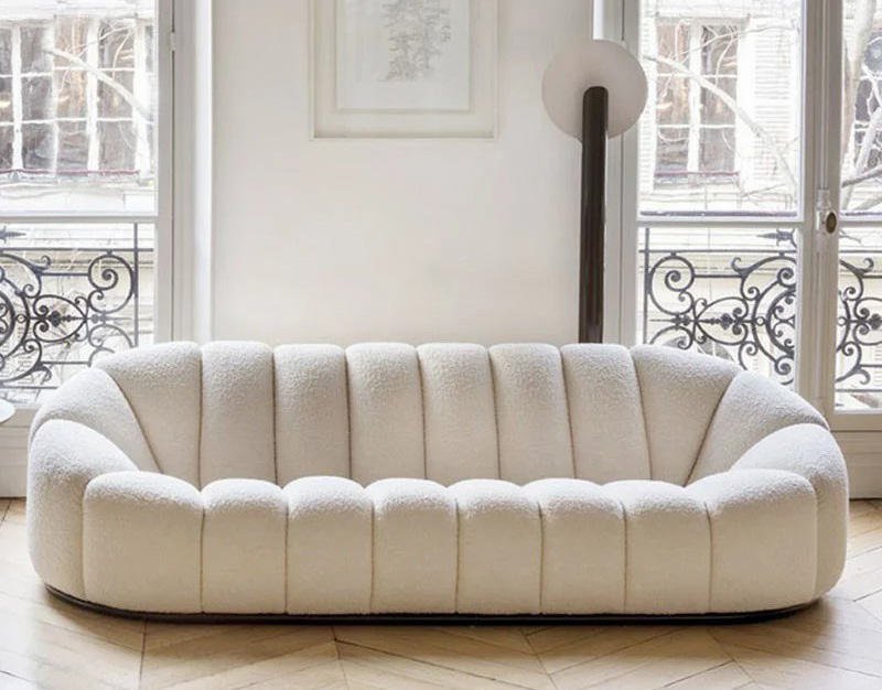Salón pequeño con sofá de estructura de madera, alfombra clara y textiles neutros